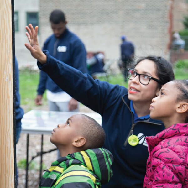 Woman in glasses and a dark blue sweatshirt points to a map and talks with children about their community.