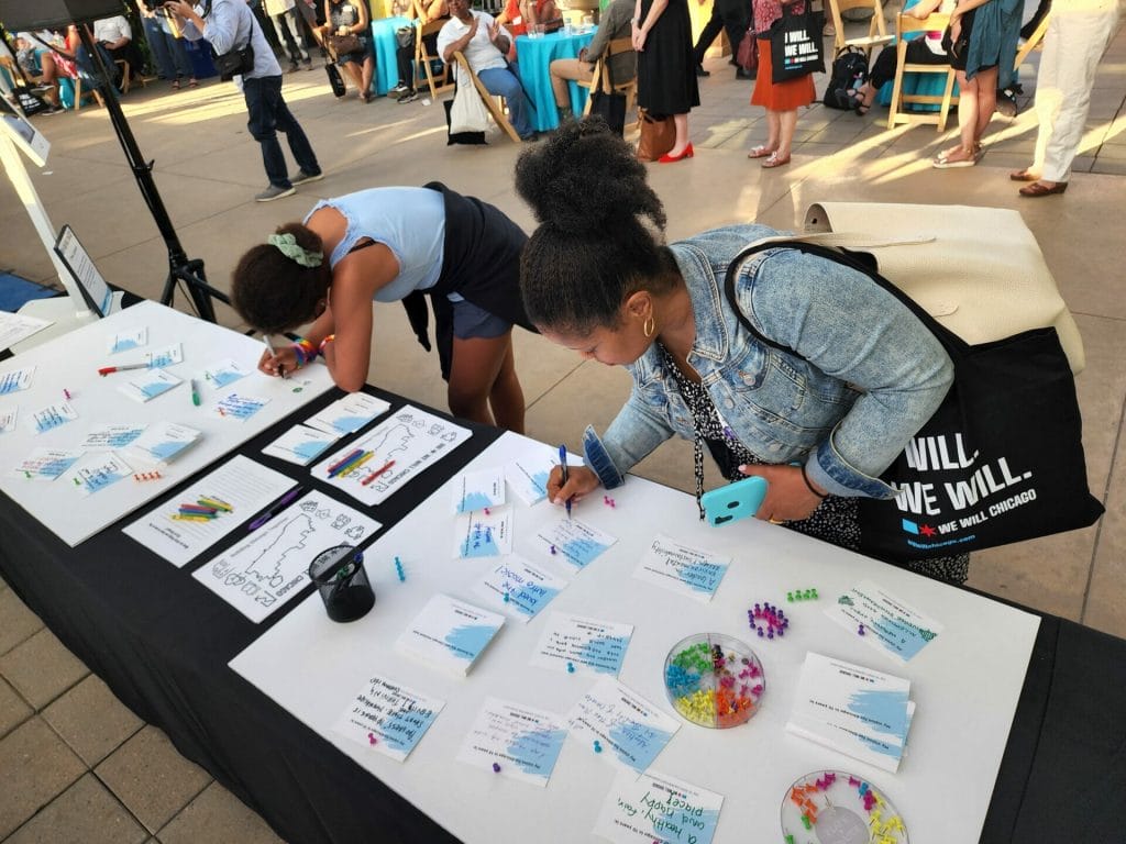 Two women write on postcards at a We Will Chicago event.